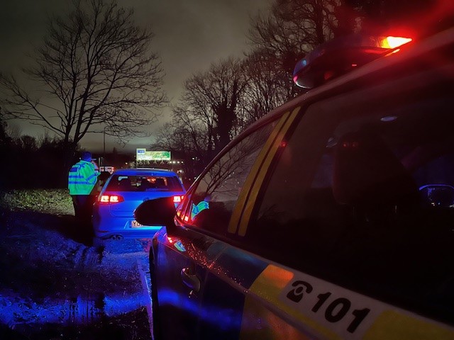 An image with the side of the police car in the foreground, and an officer speaking to the driver of another car in the background